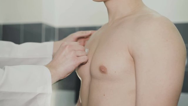 The doctor listens to a male patient via phonendoscope in clinic. 4K