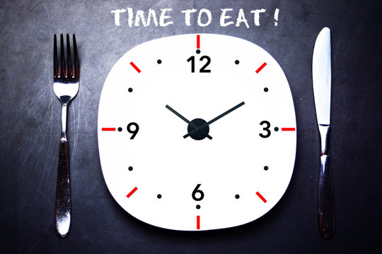 Time to eat concept with fork and knife on white plate and dark background
