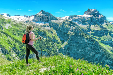 Naklejka premium girl traveler with sticks for a walk, against a backdrop of mountain peaks, admires the nature and mountain landscapes of Switzerland, the Engelberg resort