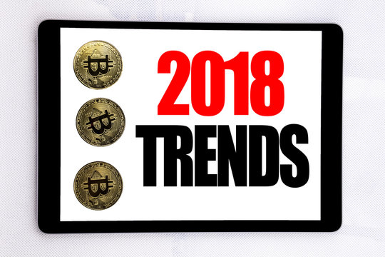 Writing text showing 2018 Trends. Business concept for Trending Data Prediction written on tablet screen on the white background with cryptocurrency bitcoin next to it.