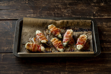 Vegetables stuffed with cheese and bacon and baked on tray in oven. Rustic recipe food on wooden background. Top view