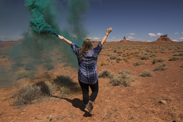 Woman with teal smoke bomb in a desert landscape on a blue sky day