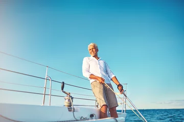 Poster Smiling mature man enjoying a day sailing on the ocean © Flamingo Images
