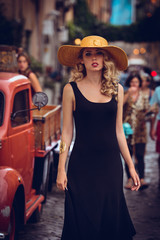 Vogue style elegant portrait of beautiful fashion woman wavy shine blonde long hair. Model in yellow summer hat black dress and luxury accessories with bright makeup at street of Trastevere Rome Italy