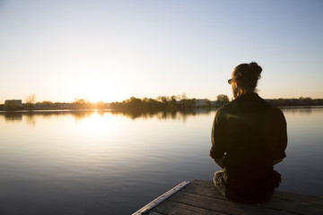 Man sits on a dock looking over still water