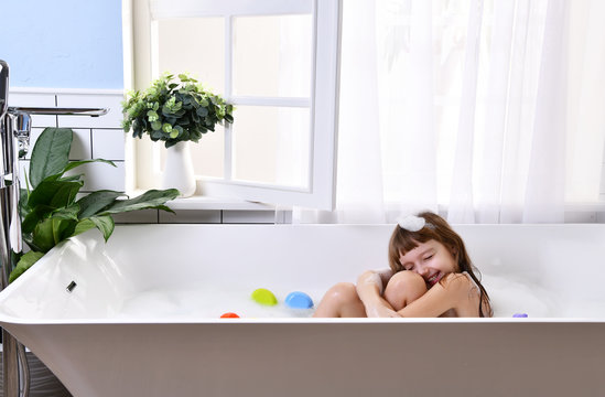  Happy little baby girl sitting in bath tub playing with duck toys  in the bathroom