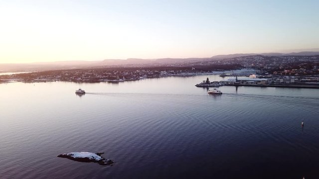 Aerial shot of two ferry boats in Oslo fjord, Norway, moving away from camera towards the sunset