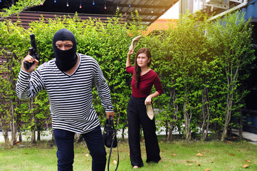 Robber wearing black hat, black and white striped shirt snatch woman's bag and run away. Woman take shoes off getting ready to throw it to him