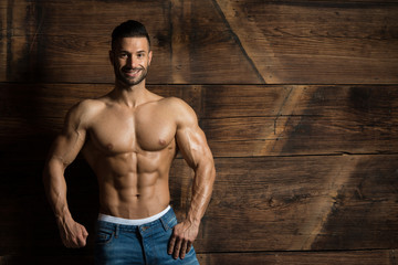 Model Flexing Muscles Against the Wooden Wall