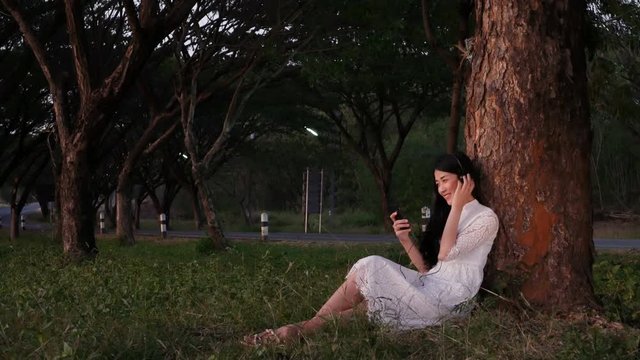 4k of woman with headphones listening to music from smart phone and sitting in the park