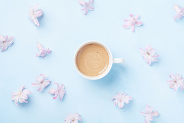 Fashion composition with morning cup of coffee and pink flowers on blue pastel background top view. Flat lay style.