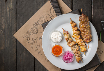 Assorted delicious grilled meat with sauces on white plate on a dark wooden background.  BBQ plate with different kinds of meat. Street fast food. Flat lay, top view.