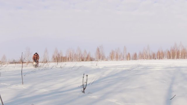 Man in winter clothes fast riding and maneuvering on mini snowmobile on deep snowdrifts in the field