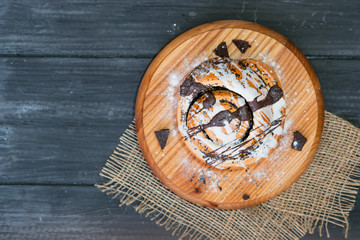 Yeast dough bun with poppy seeds and chocolate fondant on wooden Board, vintage background, top view