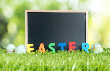 Blank blackboard with colorful easter word and paint eggs on green grass field at outdoor garden bokeh light background. Happy easter day concept.copy space for adding text.