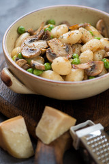 Boiled potato gnocchi with fried mushrooms and green peas served in a bowl, selective focus, vertical shot, close-up