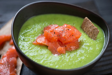 Black bowl of green peas cream-soup topped with salmon fillet, close-up, selective focus