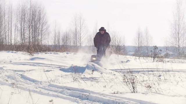 Adult man in winter clothing fast riding through the deep snow on a mini snowmobile and overcoming high snowbanks