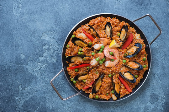Above view of spanish paella with seafood in a frying pan, view from above on a blue stone background, copyspace