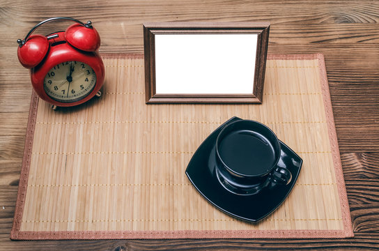 Blank photo frame with copy space, cup of black coffee and red alarm clock on office table background. Coffee break.