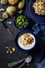 Potato soup placed with roasted croutons and fresh parsley on dark wooden background