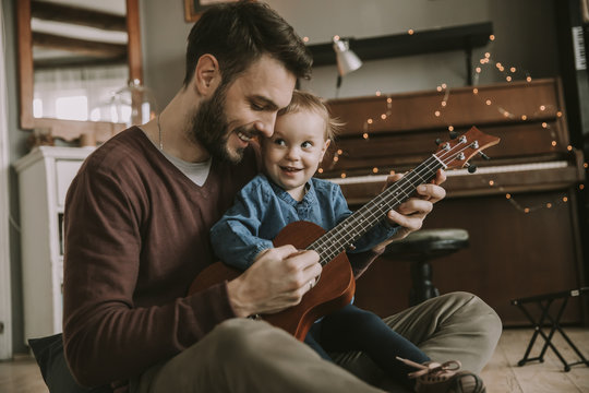 Father teaching daughter to play guitar at home