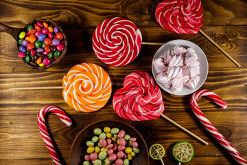 Colorful chocolate candies, lollipops, candy cane and marshmallows on wooden table