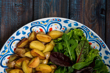 Fried baby potatoes, green salad and fresh tomatoes on a big plate in rustic style