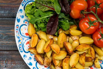 Fried baby potatoes, green salad and fresh tomatoes on a big plate in rustic style