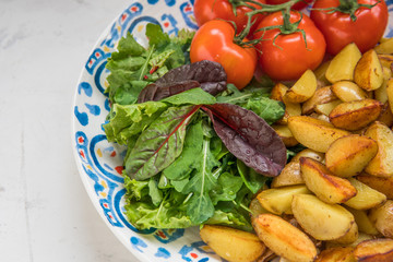 Fried baby potatoes, green salad and fresh tomatoes on a big plate in rustic style