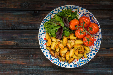Fried baby potatoes, green salad and fresh tomatoes on a big plate in rustic style