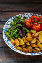 Fried baby potatoes, green salad and fresh tomatoes on a big plate in rustic style