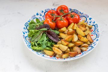 Fried baby potatoes, green salad and fresh tomatoes on a big plate in rustic style