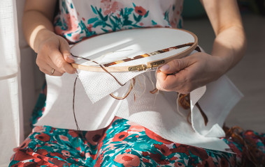 Young beautiful woman is engaged in embroidering a dagger on the embroidery frame in a colored...