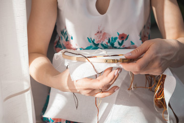 Young beautiful woman is engaged in embroidering a dagger on the embroidery frame in a colored...