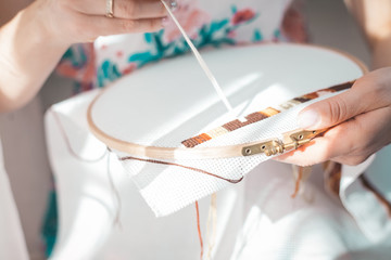 Young beautiful woman is engaged in embroidering a dagger on the embroidery frame in a colored...