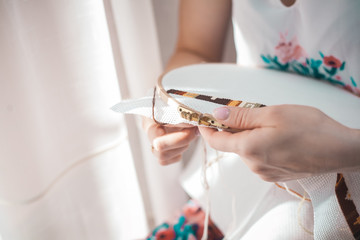 Young beautiful woman is engaged in embroidering a dagger on the embroidery frame in a colored dress at the window in the sunlight. A great picture for a hobby