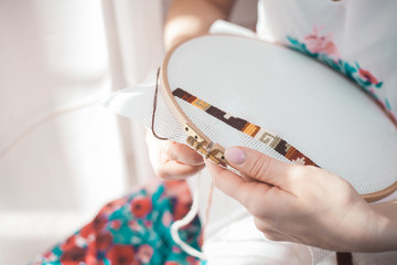 Young beautiful woman is engaged in embroidering a dagger on the embroidery frame in a colored...
