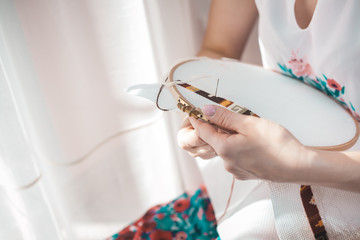 Young beautiful woman is engaged in embroidering a dagger on the embroidery frame in a colored...