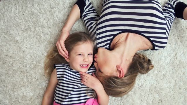 Cute girl lying on the floor with her mum, kissing each other. Tenderness and parenthood concept. 