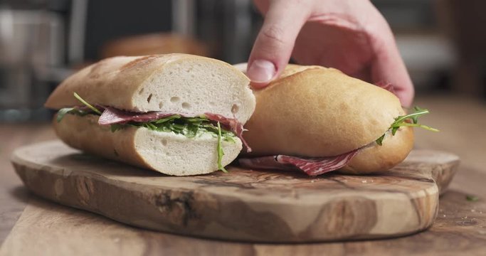 Slow motion man hands take baguette sandwich with coppa from wood board