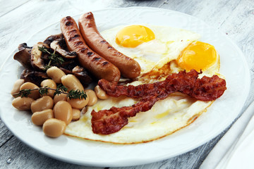 Traditional full English breakfast with fried eggs, sausages, beans, mushroomsand bacon on wooden background