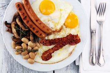 Traditional full English breakfast with fried eggs, sausages, beans, mushroomsand bacon on wooden background