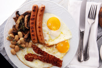 Traditional full English breakfast with fried eggs, sausages, beans, mushroomsand bacon on wooden background