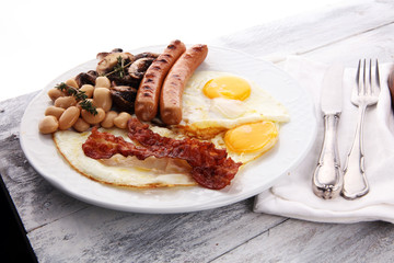 Traditional full English breakfast with fried eggs, sausages, beans, mushroomsand bacon on wooden background