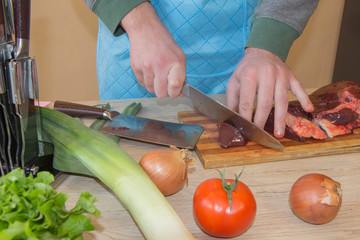 a man in a kitchen apron, meat on a board and a wooden table