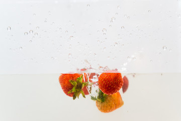 Red strawberry splashing in clear water
