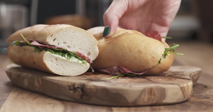 Slow motion hands take baguette sandwich with coppa from wood board