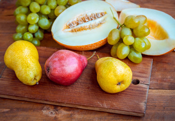 Fresh ripe red and yellow pears, juicy melon and green grape on a wooden table. Autumn fruit harvest.