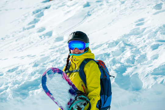 Image of smiling woman in helmet and with snowboard against background of snowy landscape